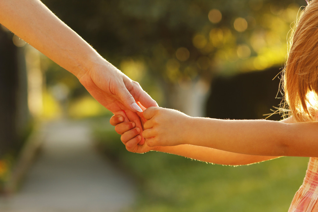 A child's hands holding a hand of a parent outdoors